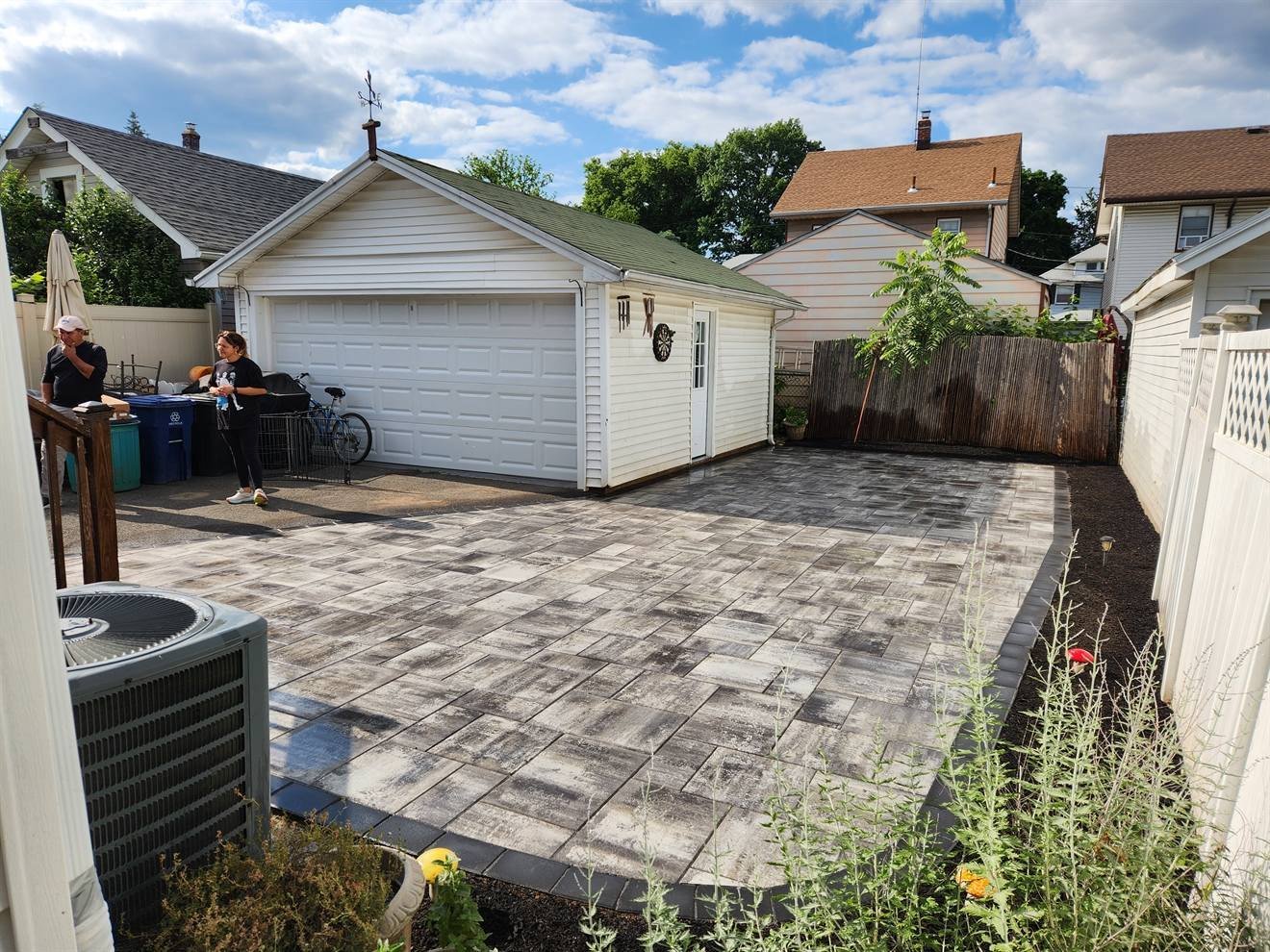 Completed gray paver patio between a home and detached garage